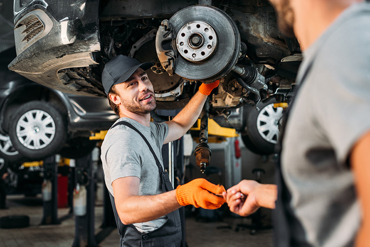 professional manual workers repairing car without wheel in mechanic shop